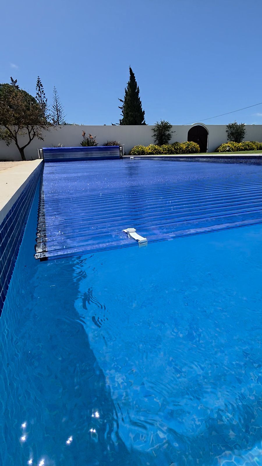 Piscina com água cristalina e cobertura automática de lâminas parcialmente aberta